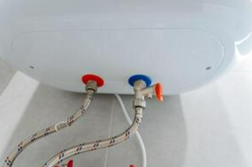 Gros plan sur un chauffe-eau blanc avec des tuyaux rouges et bleus, fixé sur un mur blanc.