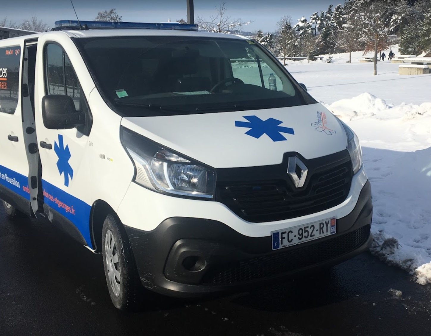 Ambulance Renault blanche avec une étoile bleue, stationnée sur un sol enneigé.
