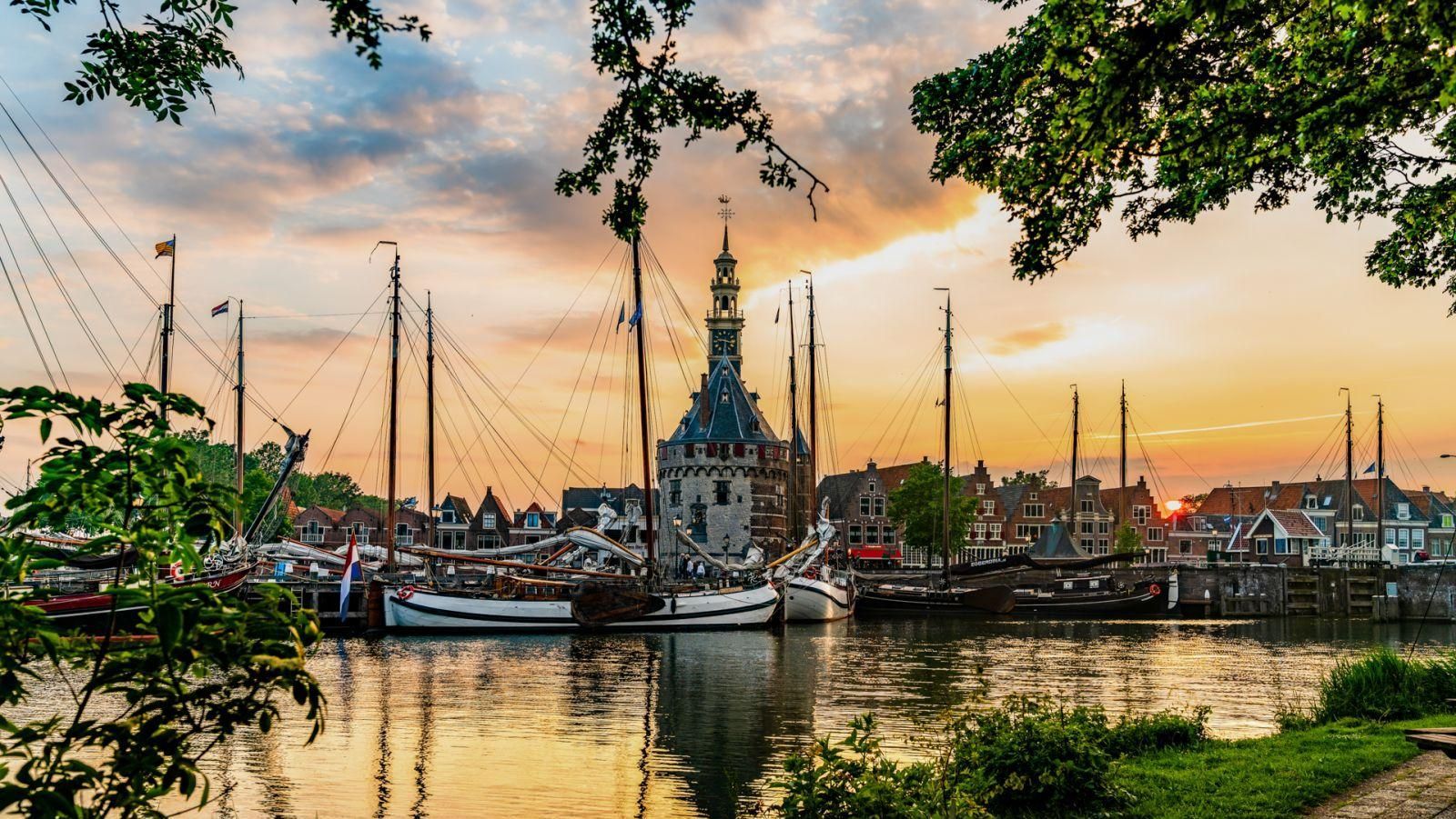 Een groep zeilboten ligt bij zonsondergang aangemeerd in een haven.