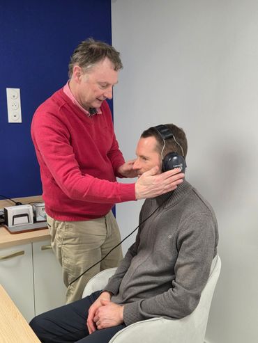 Un homme ajuste un casque audio sur une personne assise dans une salle de clinique