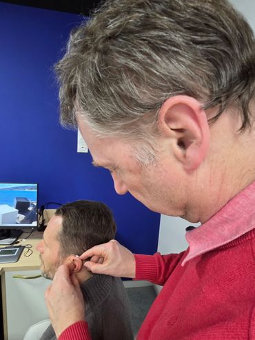 Une personne installe un écouteur sur une autre personne dans un bureau aux tons bleus.