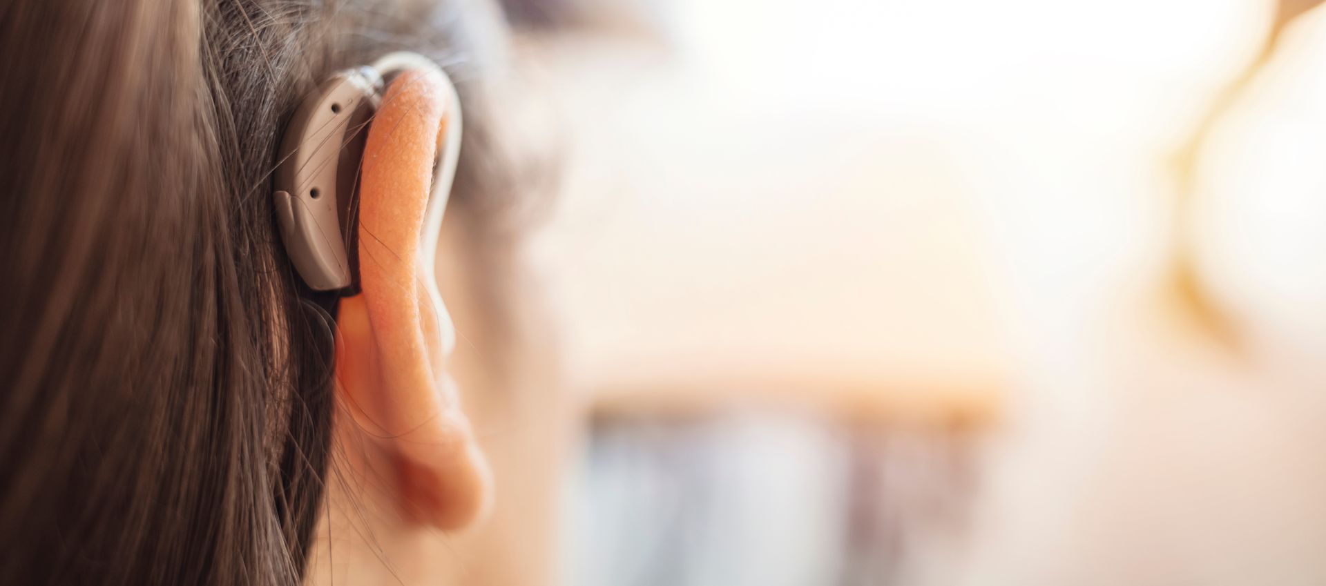 Personne portant un appareil auditif sur l'oreille, sur un fond clair flou.