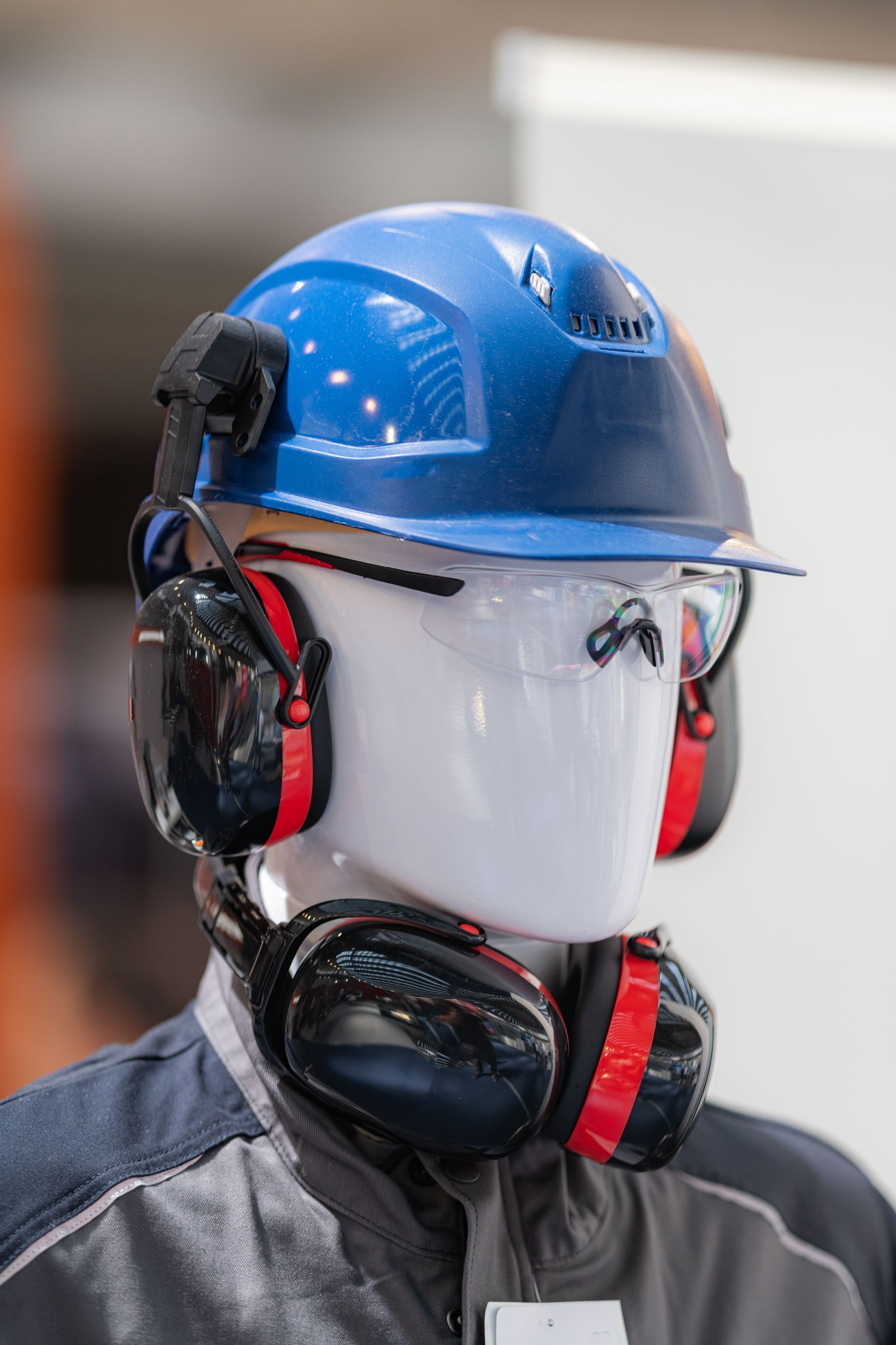 Casque de chantier bleu et protection auditive rouge et noire sur une tête de mannequin blanche dans un atelier
