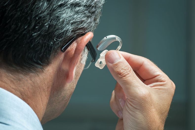 Un homme ajuste un petit appareil auditif derrière l'oreille.