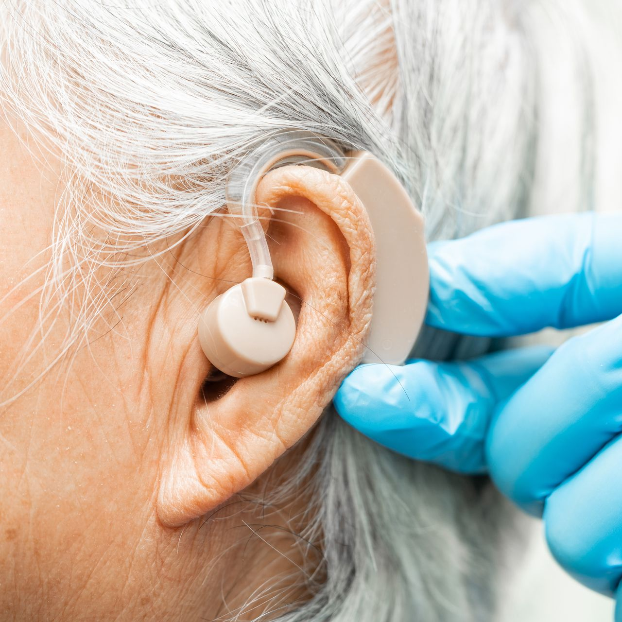 Gros plan sur un appareil auditif ajusté dans l'oreille d'une personne âgée par une main gantée