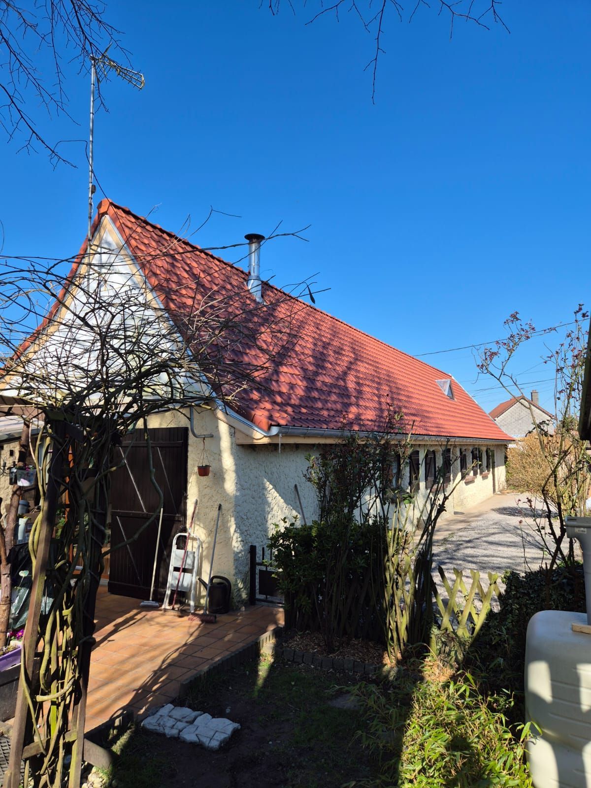 Bâtiment beige avec toit rouge, cheminée et antenne.