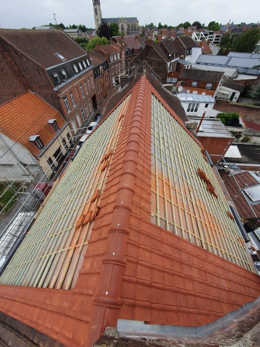Vue d'un toit de tuiles rouges en construction, entouré de bâtiments dans une ville européenne.