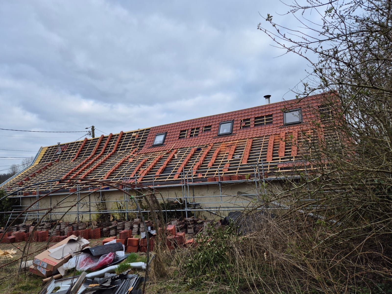 Toiture partiellement recouverte de tuiles rouges ; échafaudages, puits de lumière et débris.