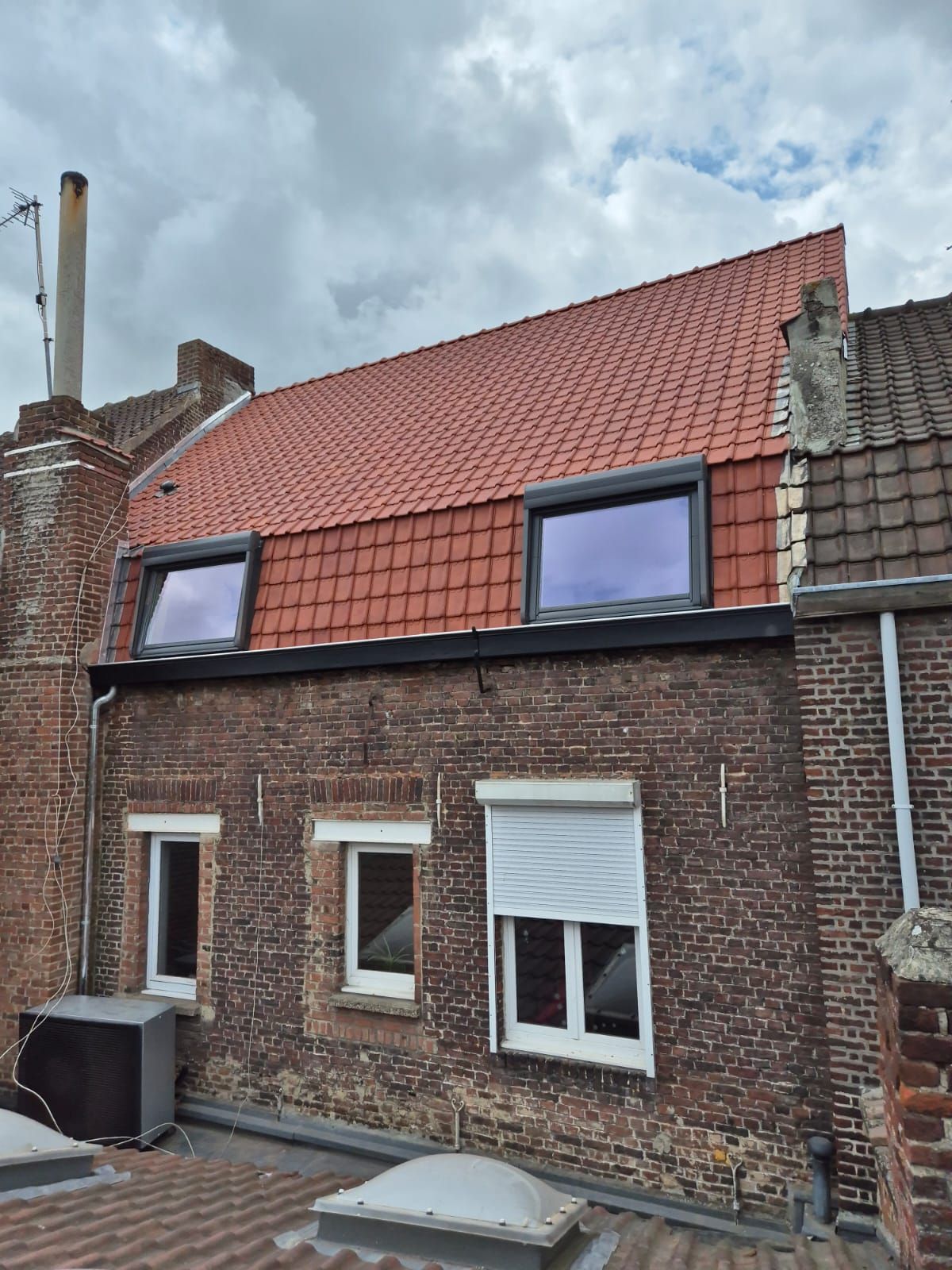 Bâtiment en briques avec toit de tuiles rouges, deux lucarnes et trois fenêtres en dessous.