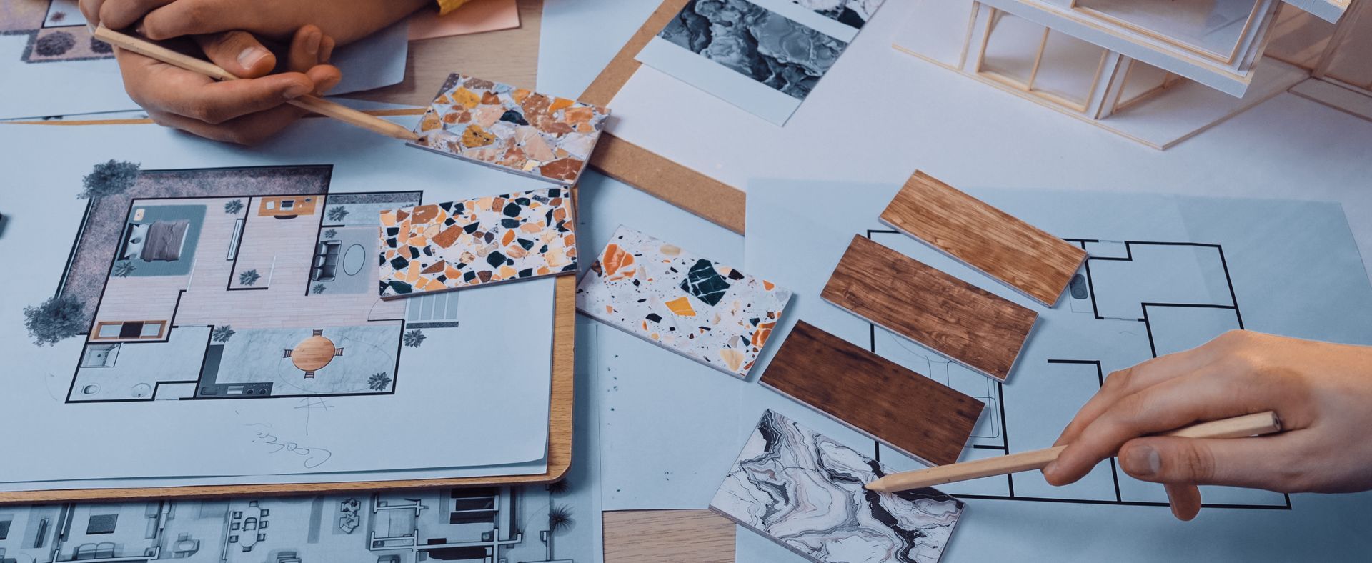 Des mains pointent du doigt des échantillons de design et des plans architecturaux posés sur une table.