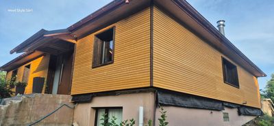 Un ouvrier du bâtiment, coiffé d'un casque blanc, est accroupi sur un revêtement de toit en contreplaqué, en train de clouer des chevrons par une journée ensoleillée.
