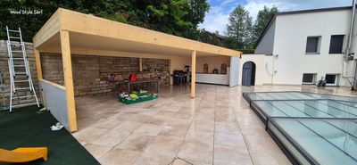 Une terrasse moderne sur le toit avec une terrasse en bois, un coin salon couvert avec des meubles gris et une jardinière surélevée avec des arbres.