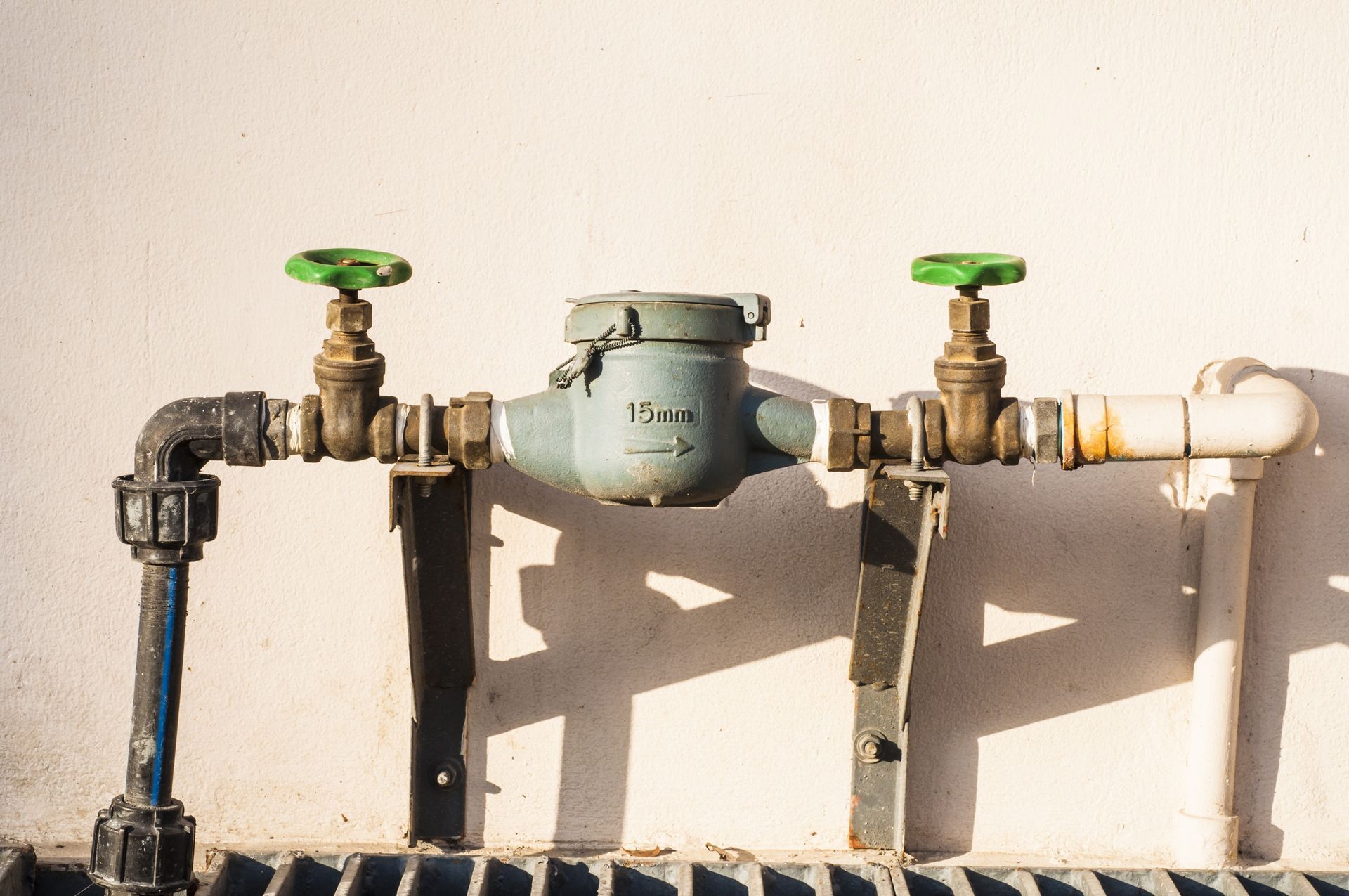 Contador de agua con válvulas verdes en una pared blanca.