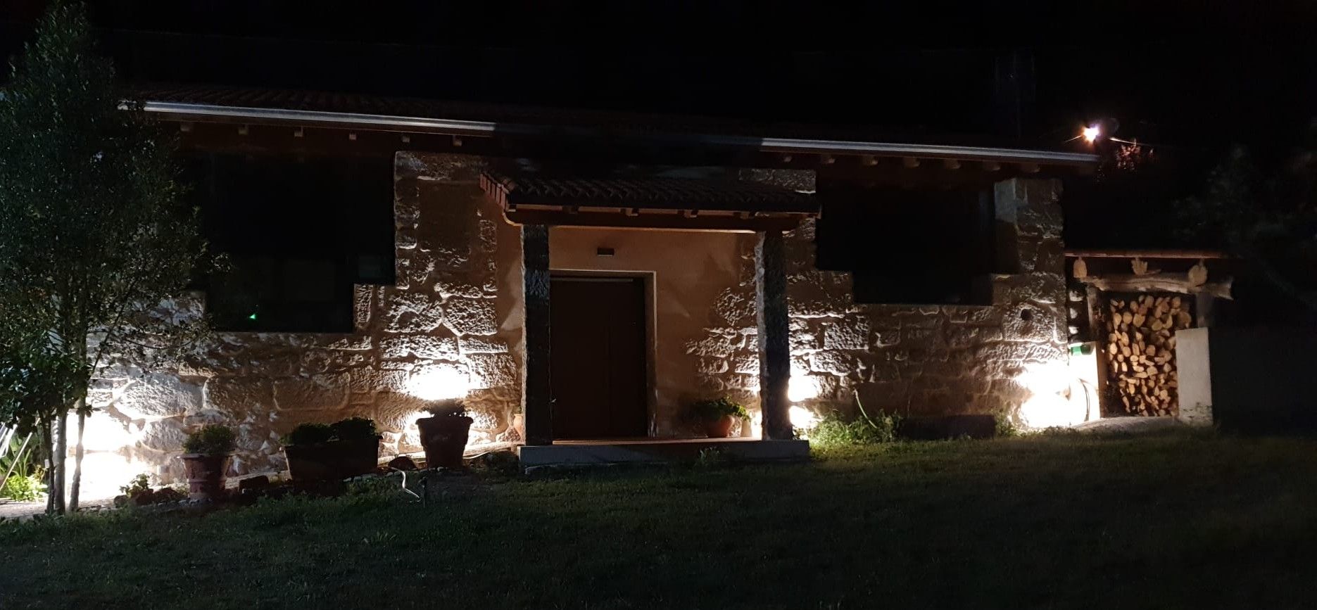 Casa de piedra iluminada por la noche con una pila de leña en el lado derecho.