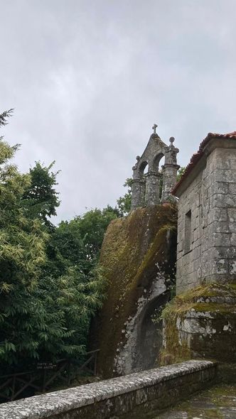 Iglesia de piedra sobre una gran formación rocosa; follaje verde, cielo nublado.