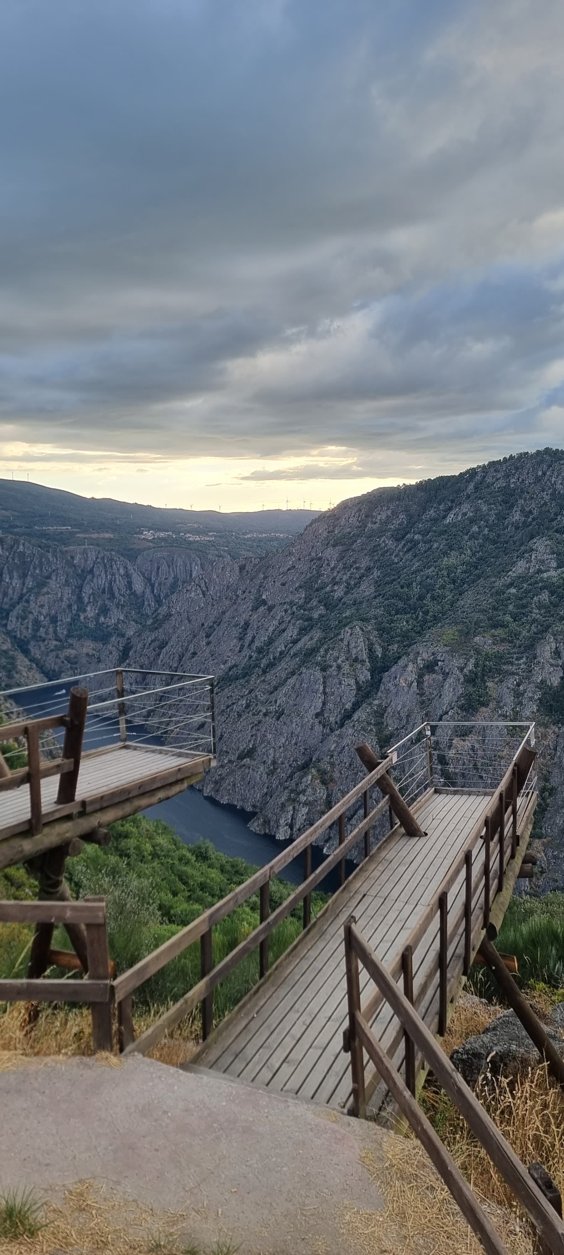 Pasarelas de madera se extienden sobre un profundo cañón con un río debajo, bajo un cielo nublado.