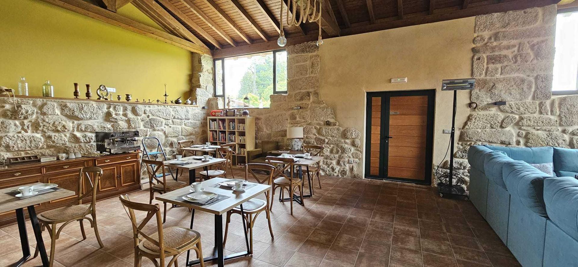 Interior de un restaurante rústico con paredes de piedra, techo de madera y mesas de comedor.