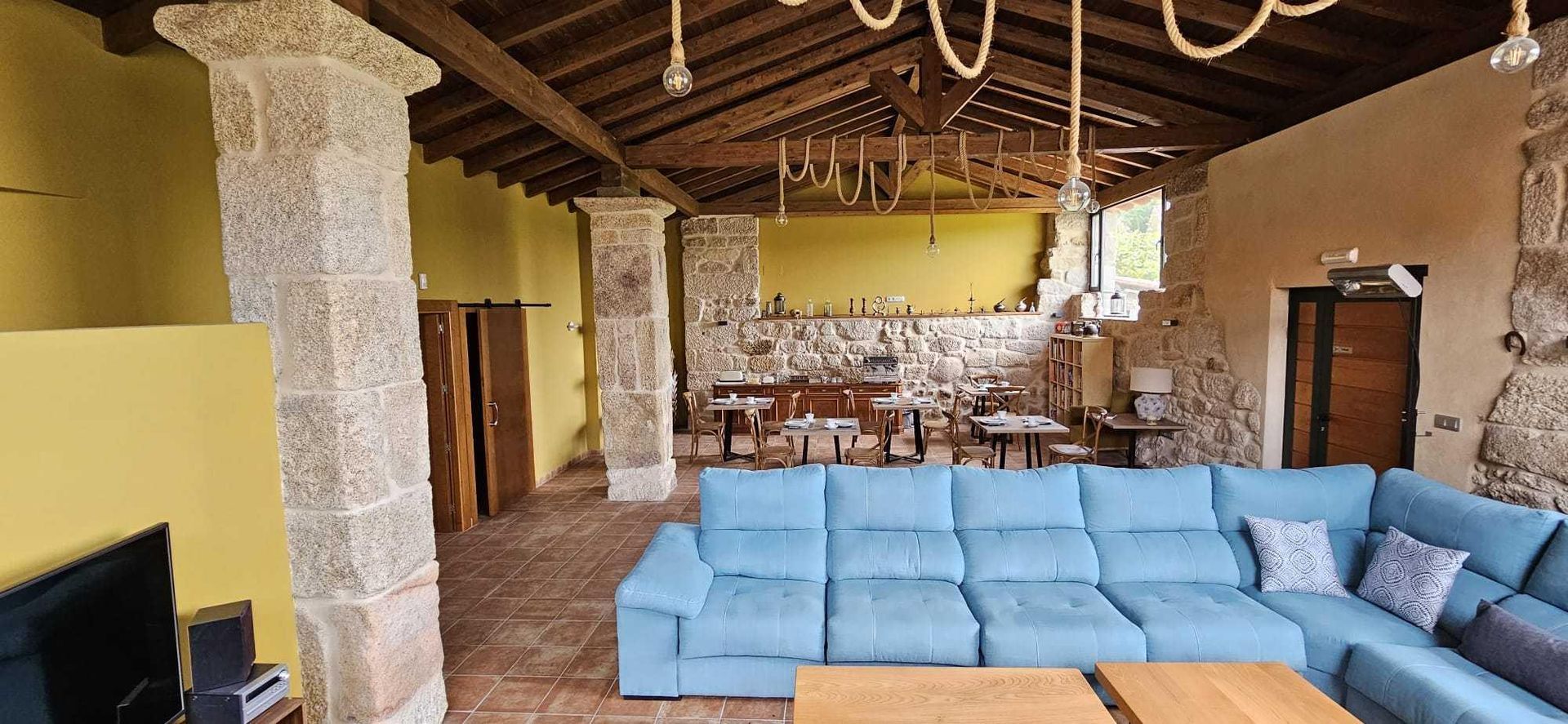 Amplia sala de estar con columnas de piedra, un sofá seccional azul y un techo de madera.