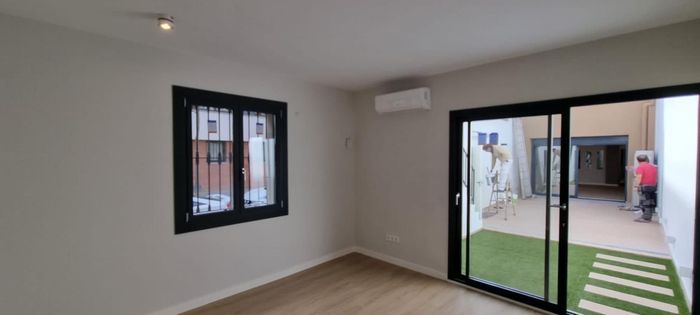 Vista interior con ventana y puerta corrediza de vidrio que da a un patio con césped. Aire acondicionado montado en la pared.