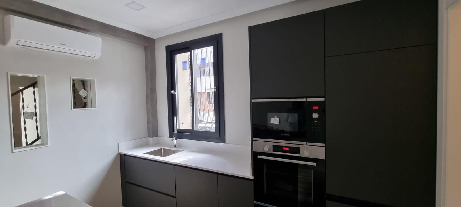 Cocina moderna con gabinetes oscuros, electrodomésticos empotrados y una ventana sobre la encimera.