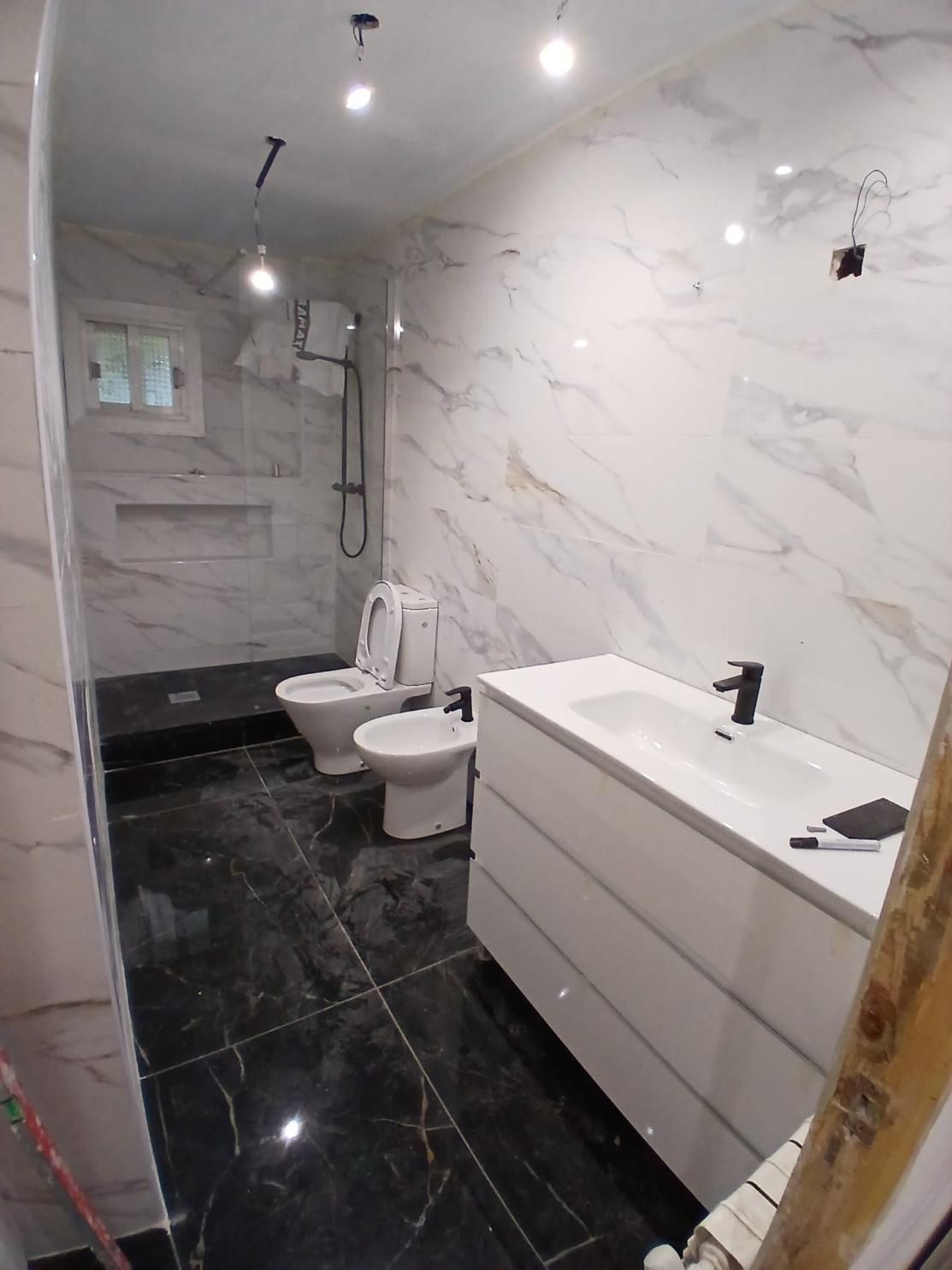 Baño moderno con paredes de mármol blanco, baldosas negras y accesorios blancos.