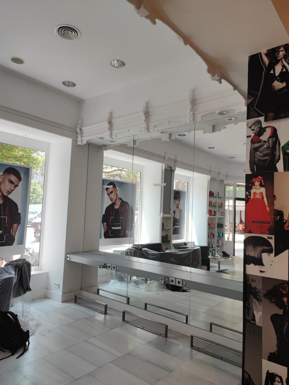 Interior de peluquería con grandes espejos, estaciones de peinado y carteles promocionales.