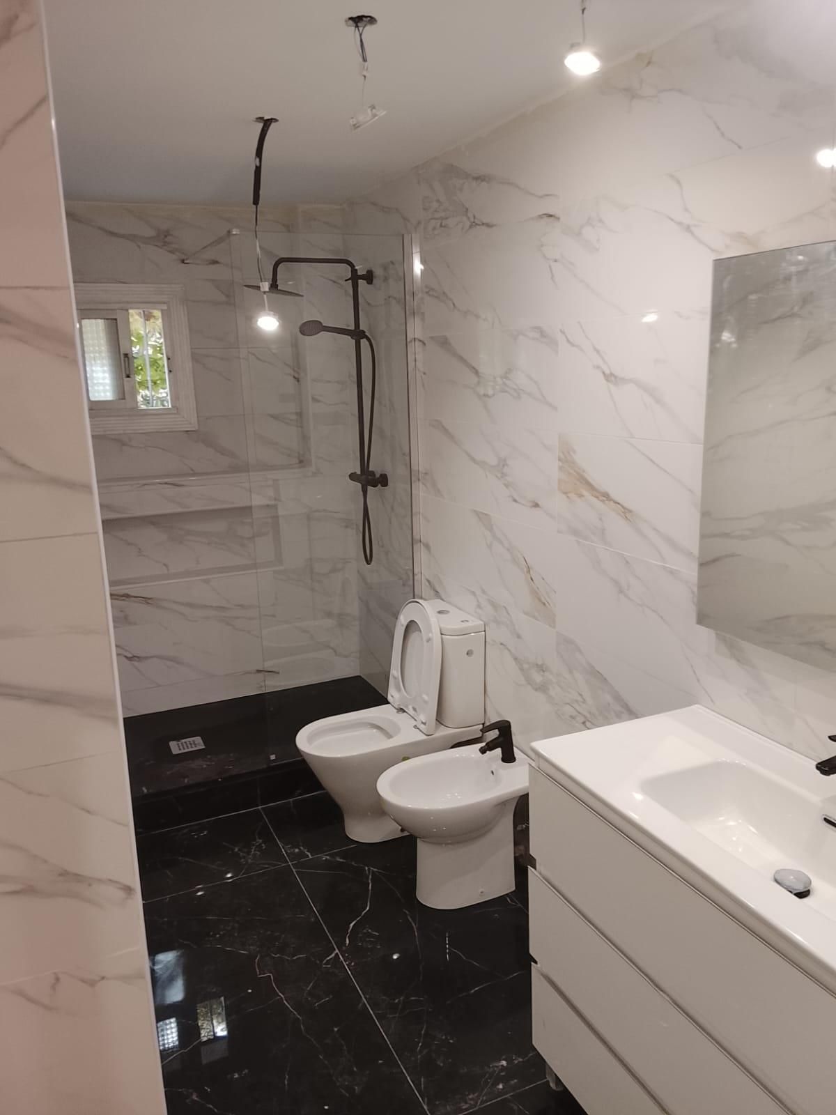 Baño moderno con paredes de mármol y suelo de baldosas negras, ducha, inodoro, bidé y lavabo.