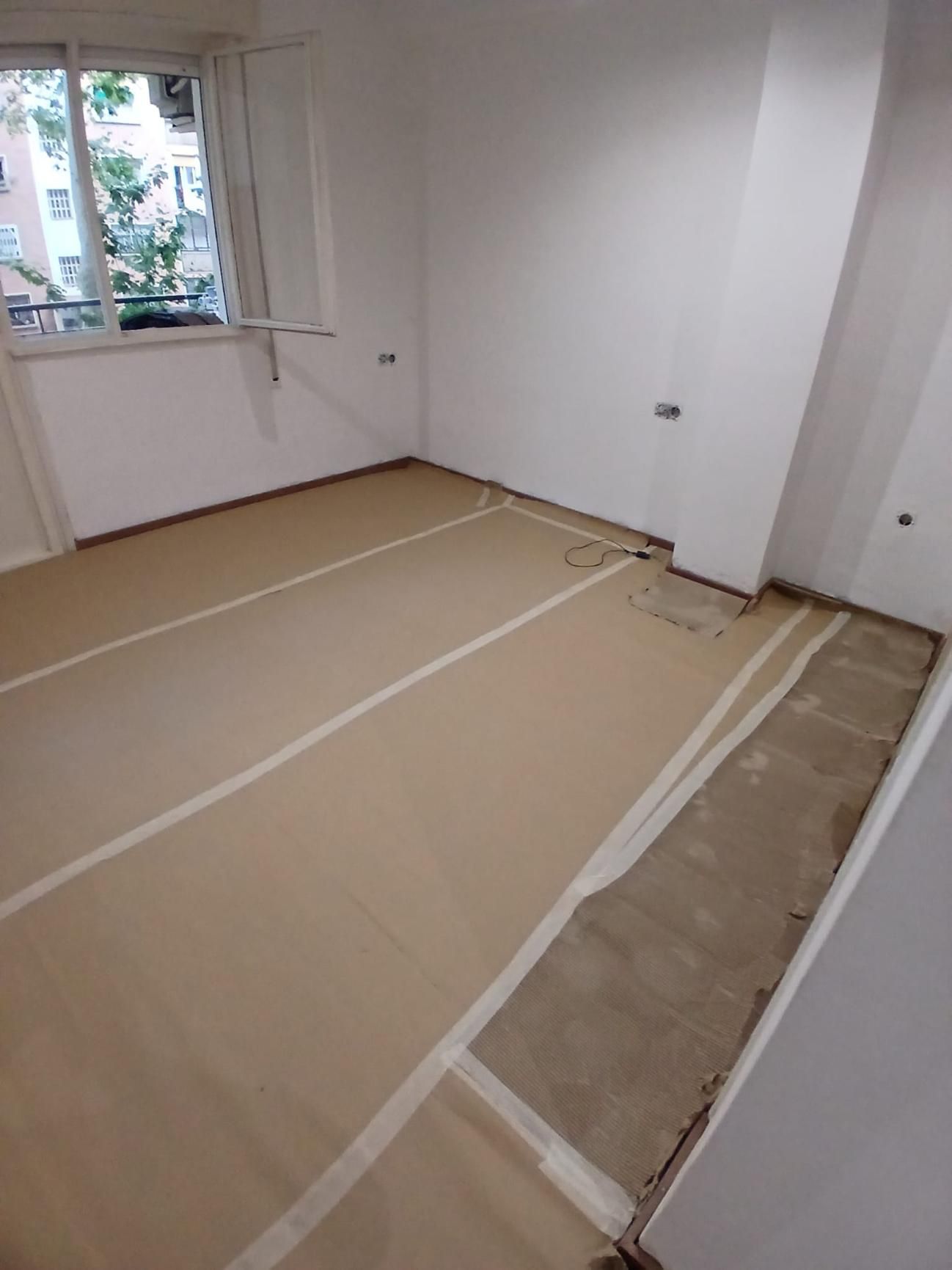 Habitación con suelo color canela, revestido con tiras blancas, cerca de una ventana. Paredes blancas.