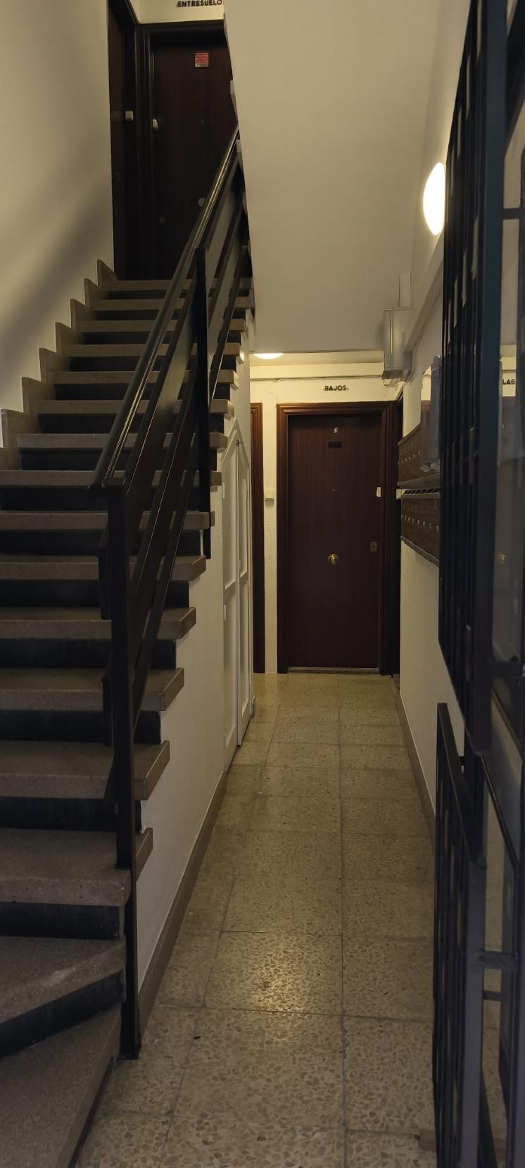 Hueco de escalera en un edificio con escaleras a la izquierda y un pasillo con puertas.