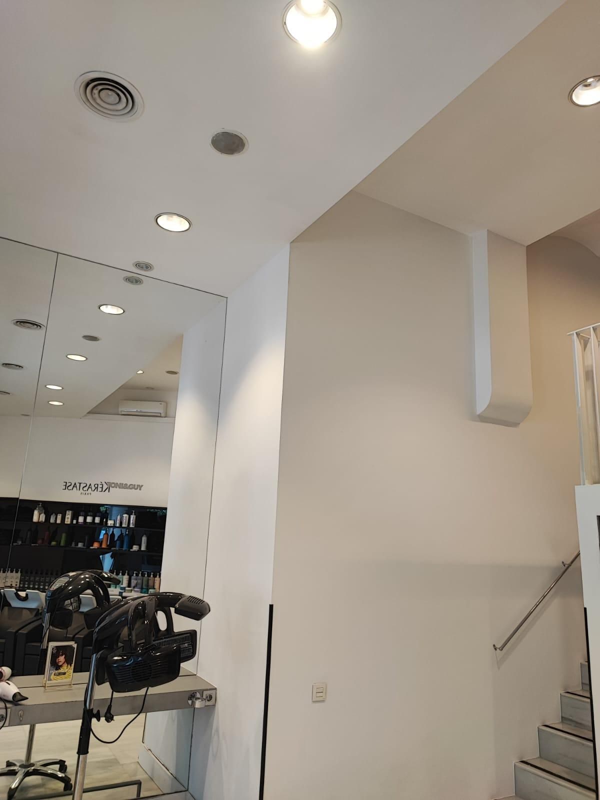 Interior de un salón con paredes blancas, espejos, luces y una escalera.