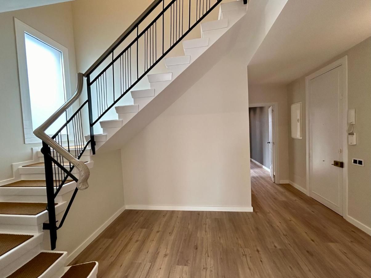 Escalera con barandilla negra y escalones blancos, que conduce a un pasillo con suelo de madera.