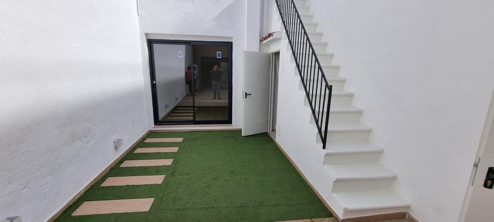 Un pequeño espacio al aire libre con césped verde, escalones de piedra, una escalera blanca y una puerta.