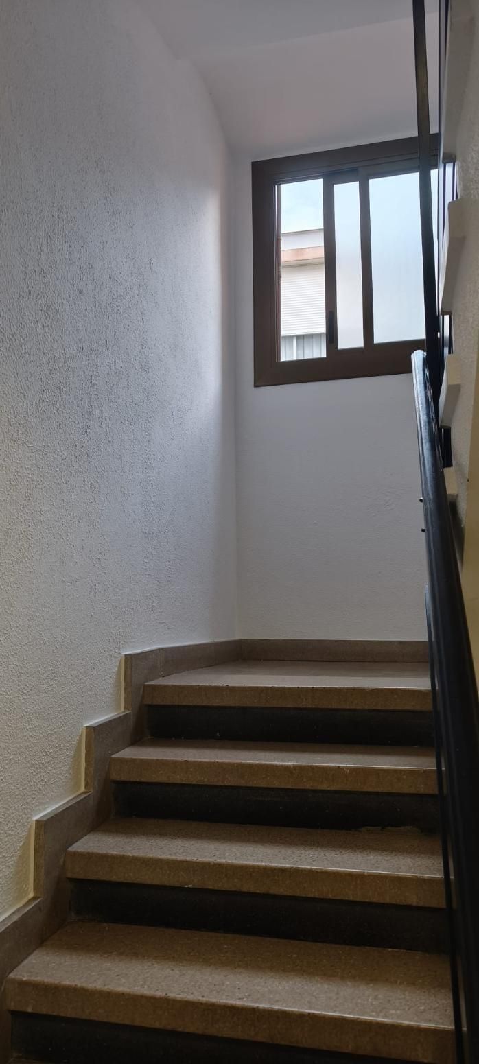 Escalera con escalones de mármol que conduce a una ventana. Las paredes son texturizadas y blancas. 