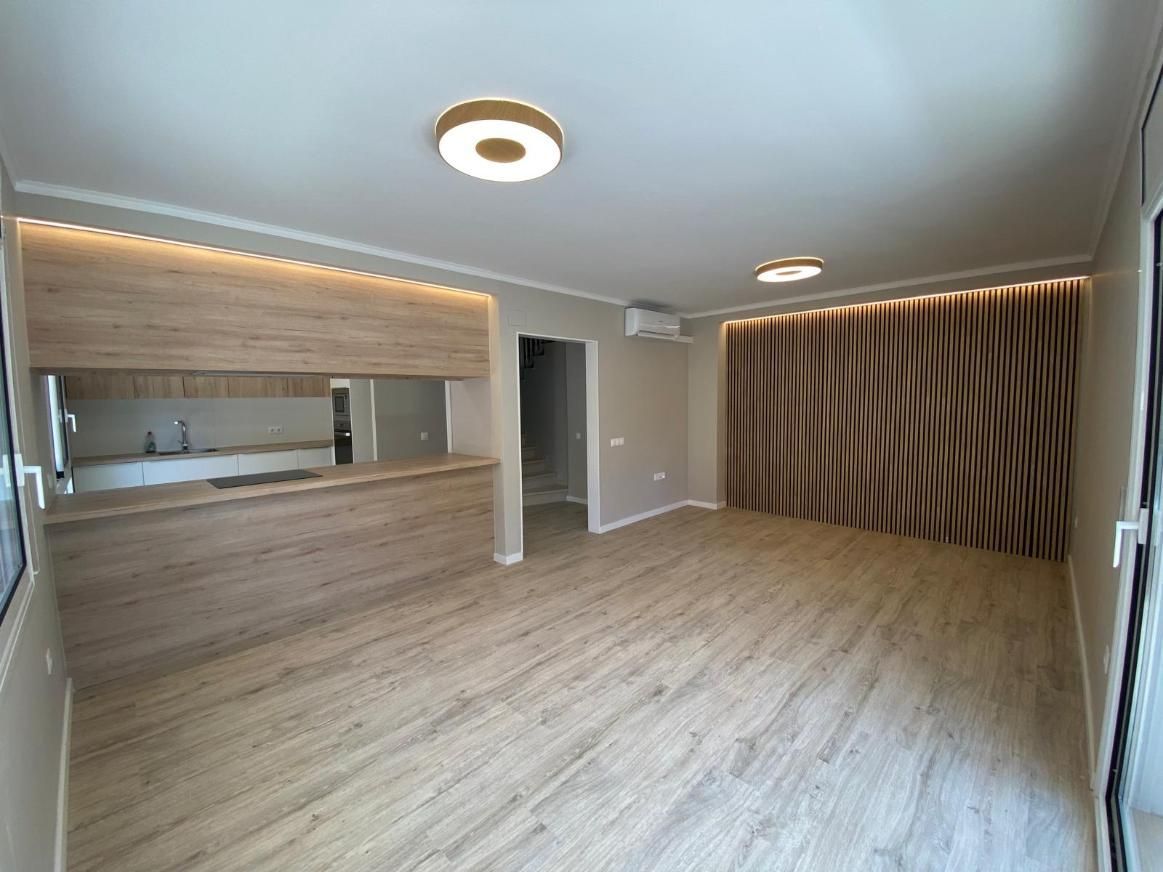 Espacio habitable vacío con detalles de madera, iluminación empotrada y área de cocina.