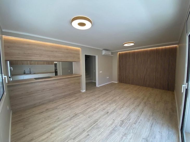 Espacio habitable vacío con detalles de madera, iluminación empotrada y área de cocina.