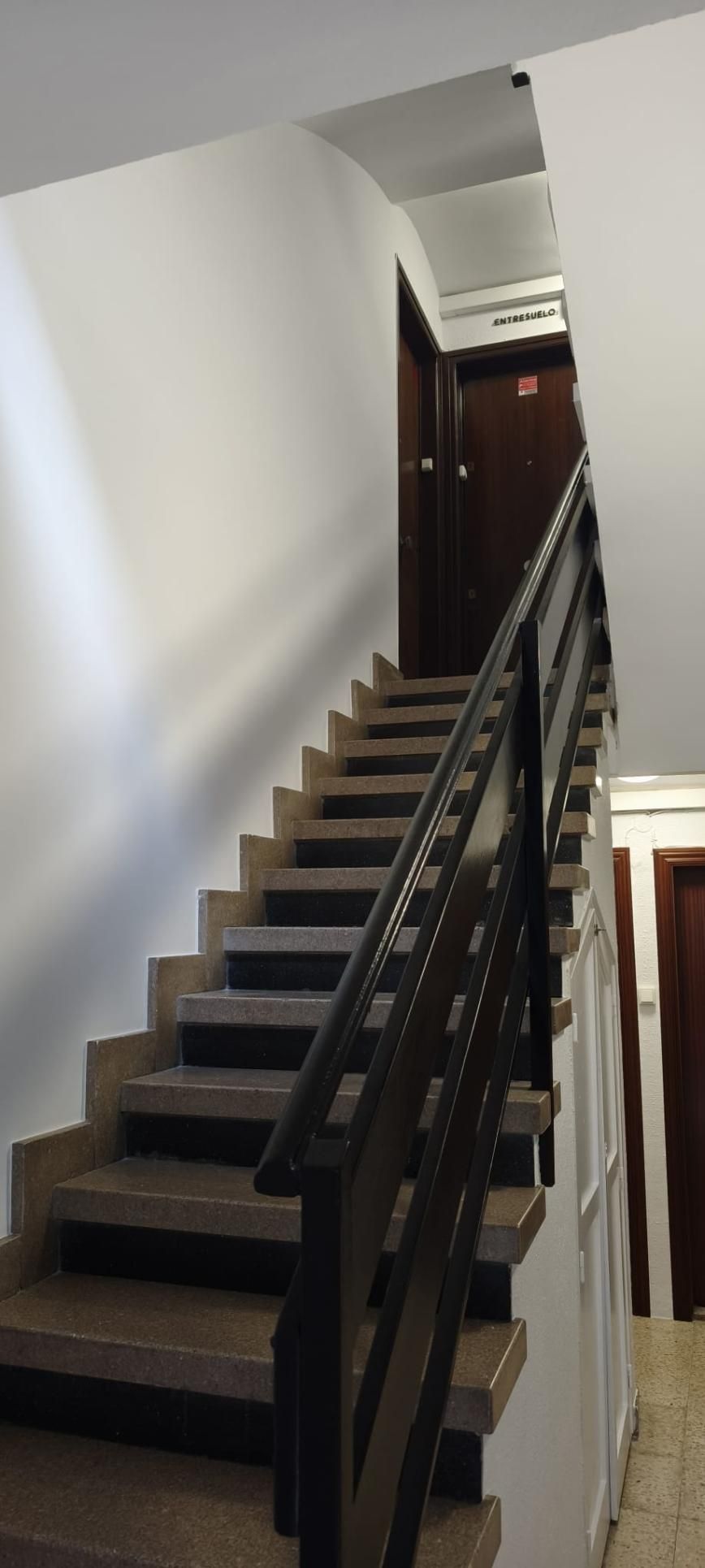 Escalera en un edificio con pasamanos de madera oscura que conduce a las puertas. Paredes blancas.