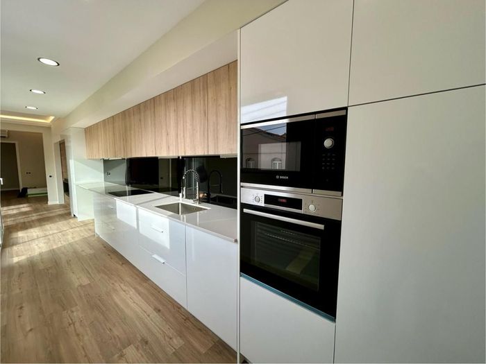Cocina blanca moderna con detalles en madera, que incluye horno y microondas empotrados.