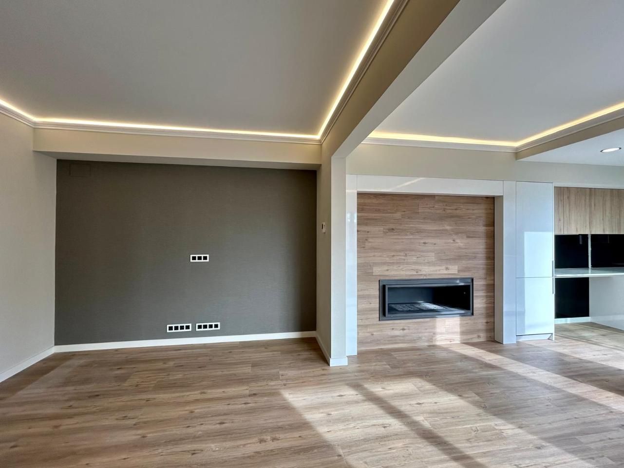 Habitación moderna con pisos de madera, iluminación empotrada y una chimenea con una pared con detalles en veta de madera.