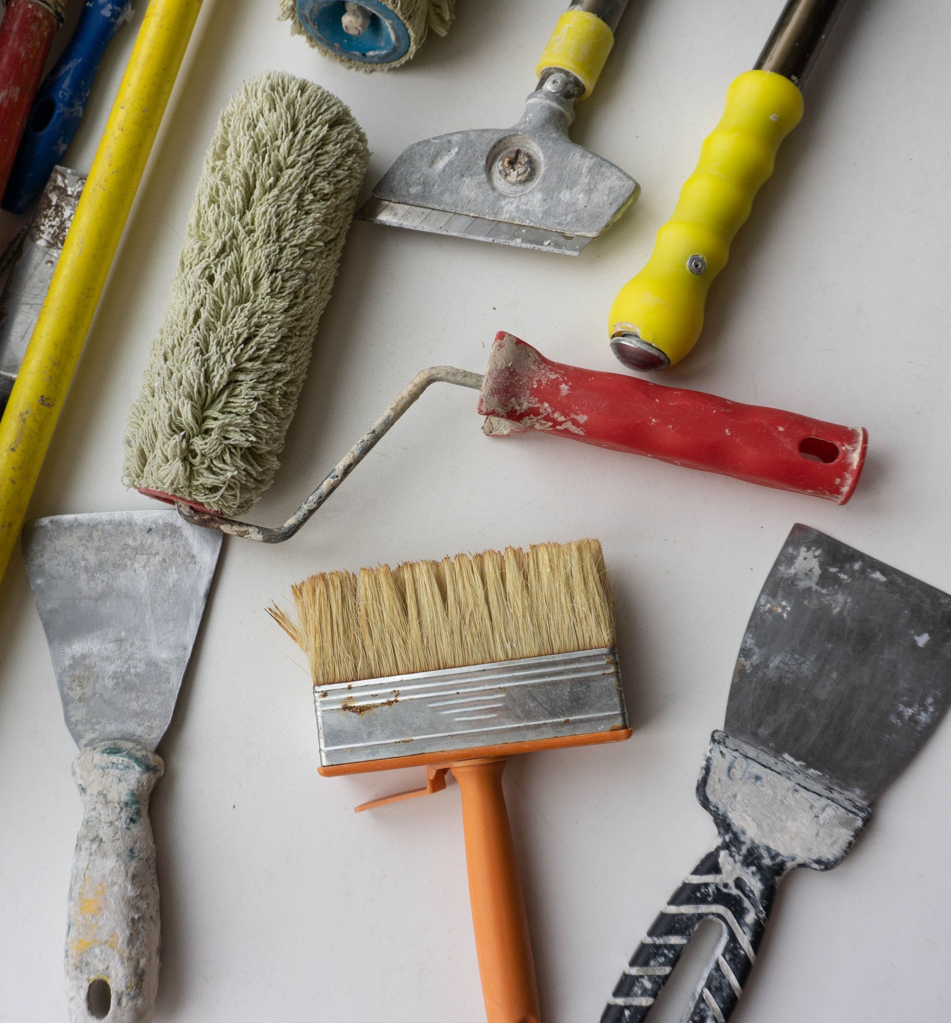 Outils pour peindre sur une surface blanche : rouleaux à peinture, grattoirs et pinceau.