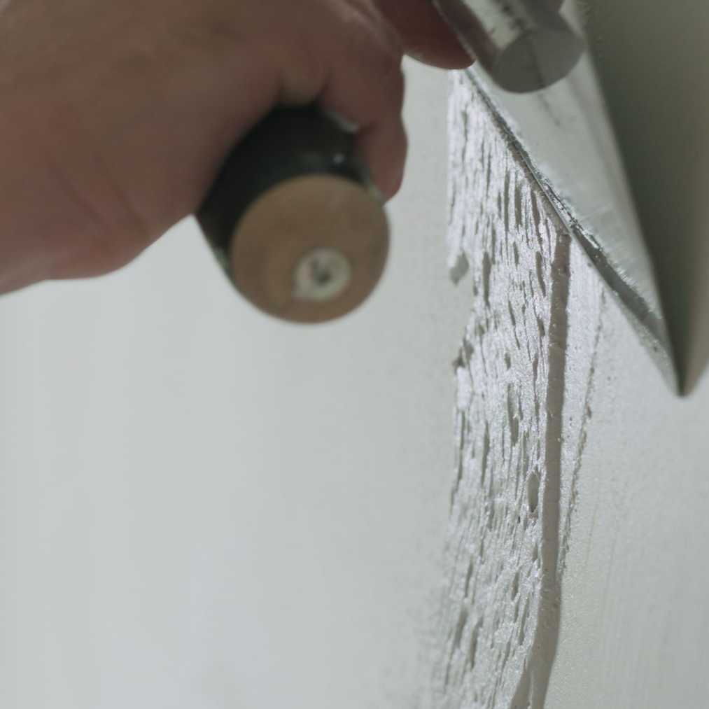 Une main utilise une truelle pour appliquer une substance grise sur une surface blanche.