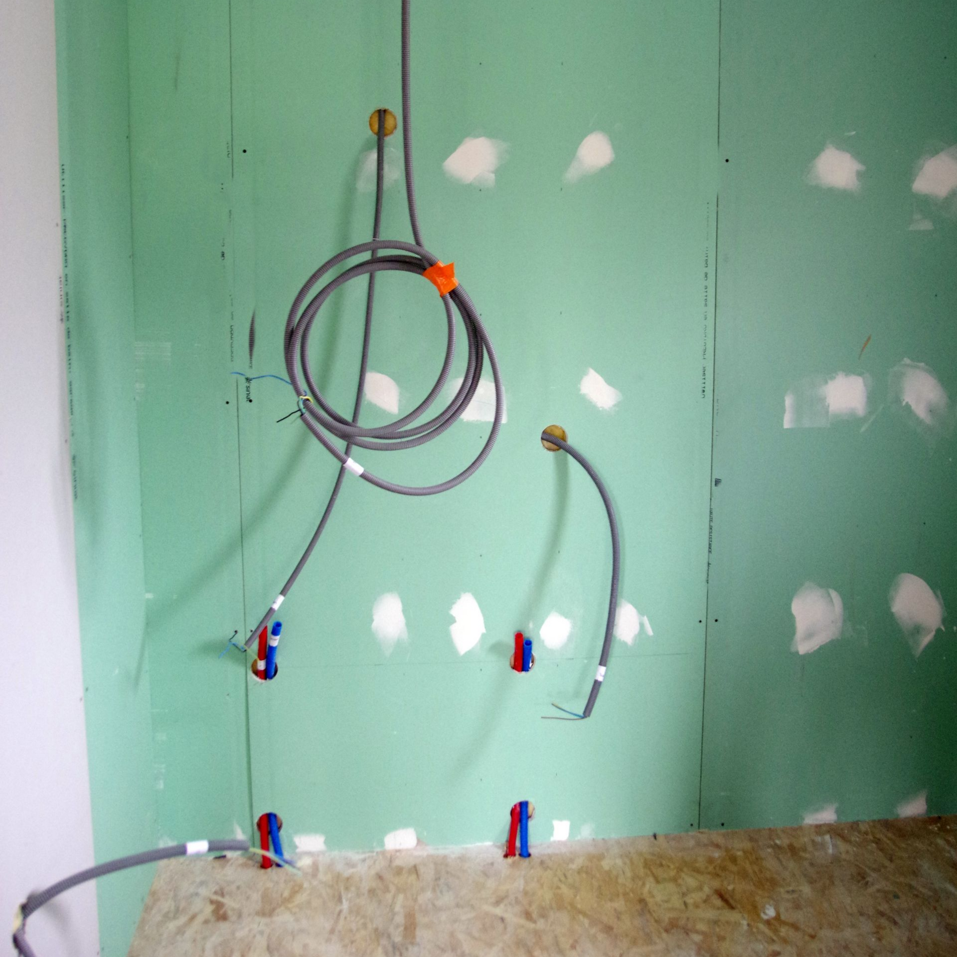 Installation de câblage électrique et de plomberie contre un mur végétal, lors de travaux de construction ou de rénovation.