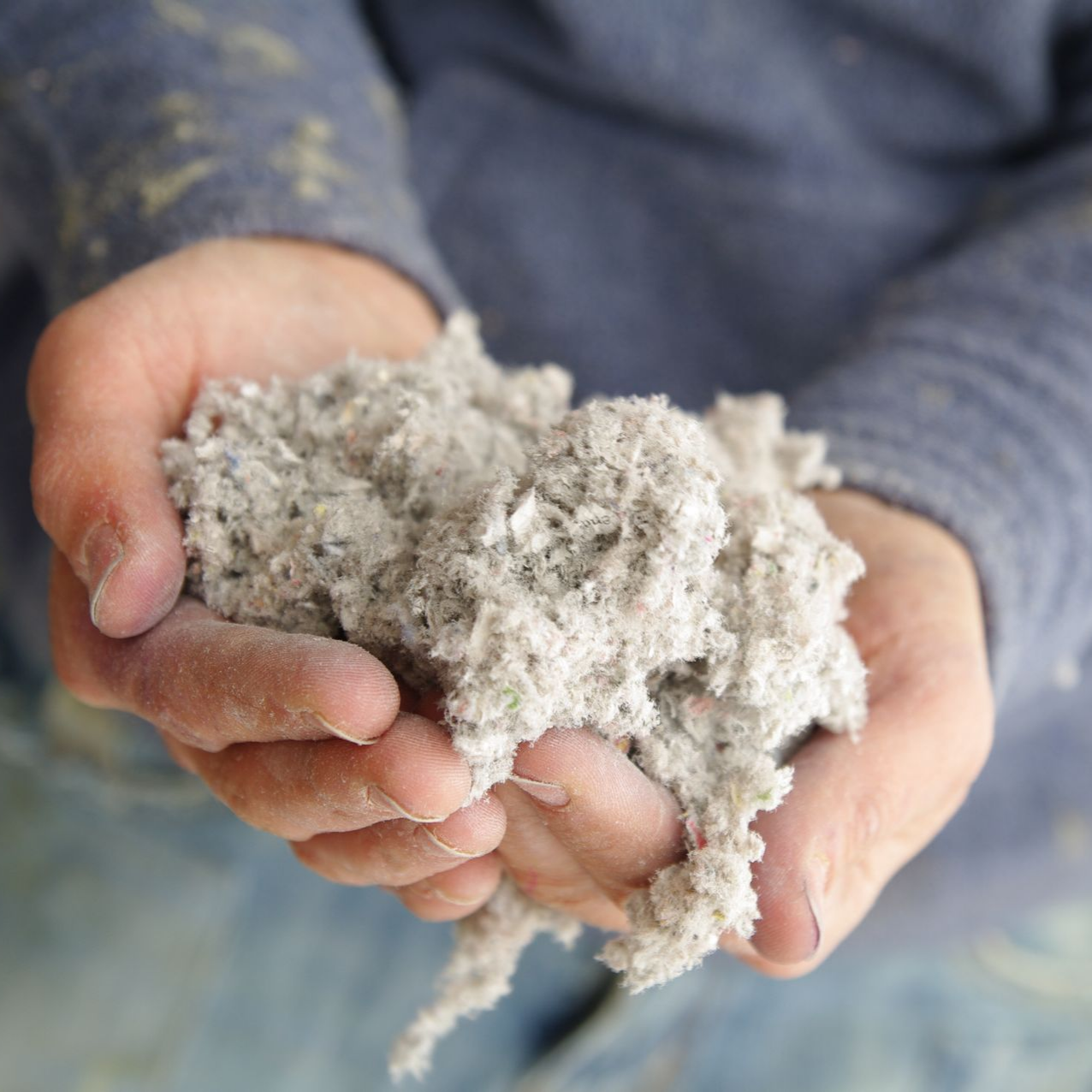 Des mains tenant une matière grise et fibreuse.