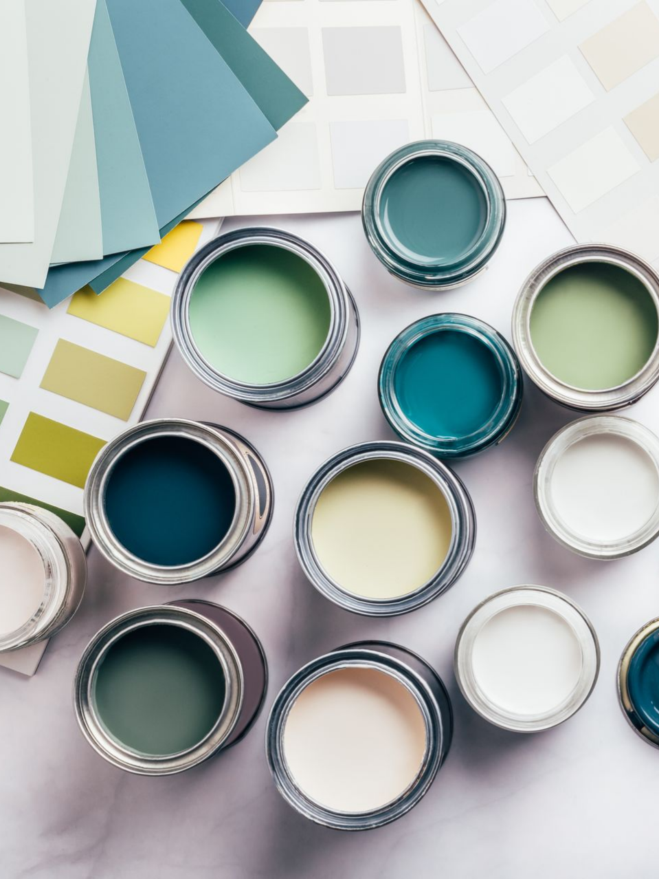 Des pots de peinture de différentes nuances de bleu, de vert et de blanc, avec des échantillons de couleur sur une surface blanche.