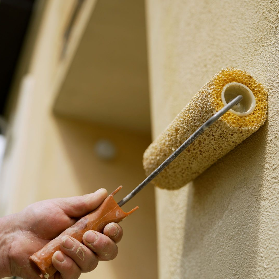Peindre à la main un mur texturé avec un rouleau à peinture jaune.