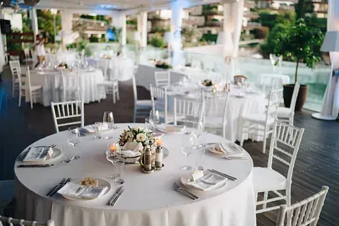 Mesas blancas preparadas para una recepción de boda, con flores y cubiertos, en un patio.