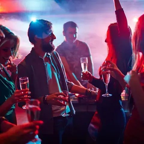 Gente de fiesta en una discoteca, con champán. Luces de colores y un DJ de fondo.