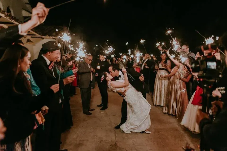 Una pareja de novios se besa mientras los invitados agitan bengalas por la noche.
