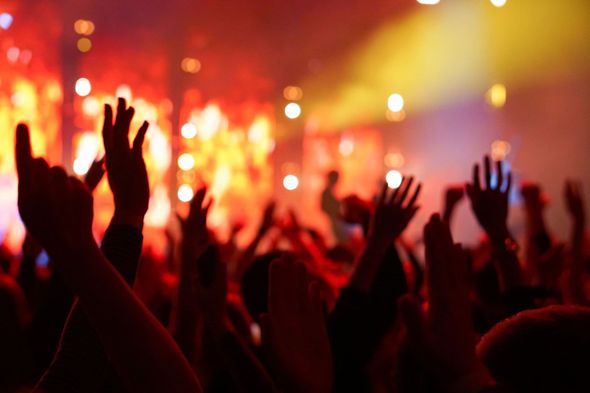Multitud con las manos levantadas en un concierto, recortadas contra las coloridas luces del escenario.