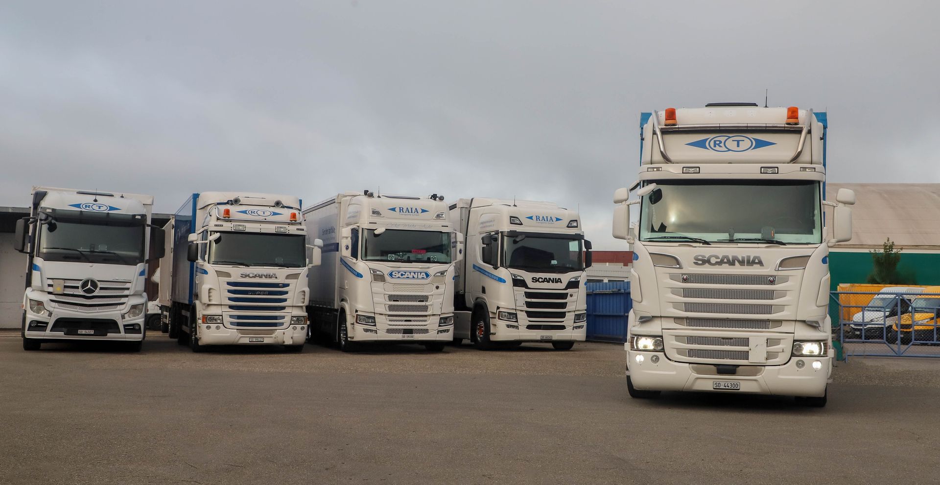 Ein weisser Lastwagen mit einem blauen Müllcontainer hebt den Container in einem Hof an.
