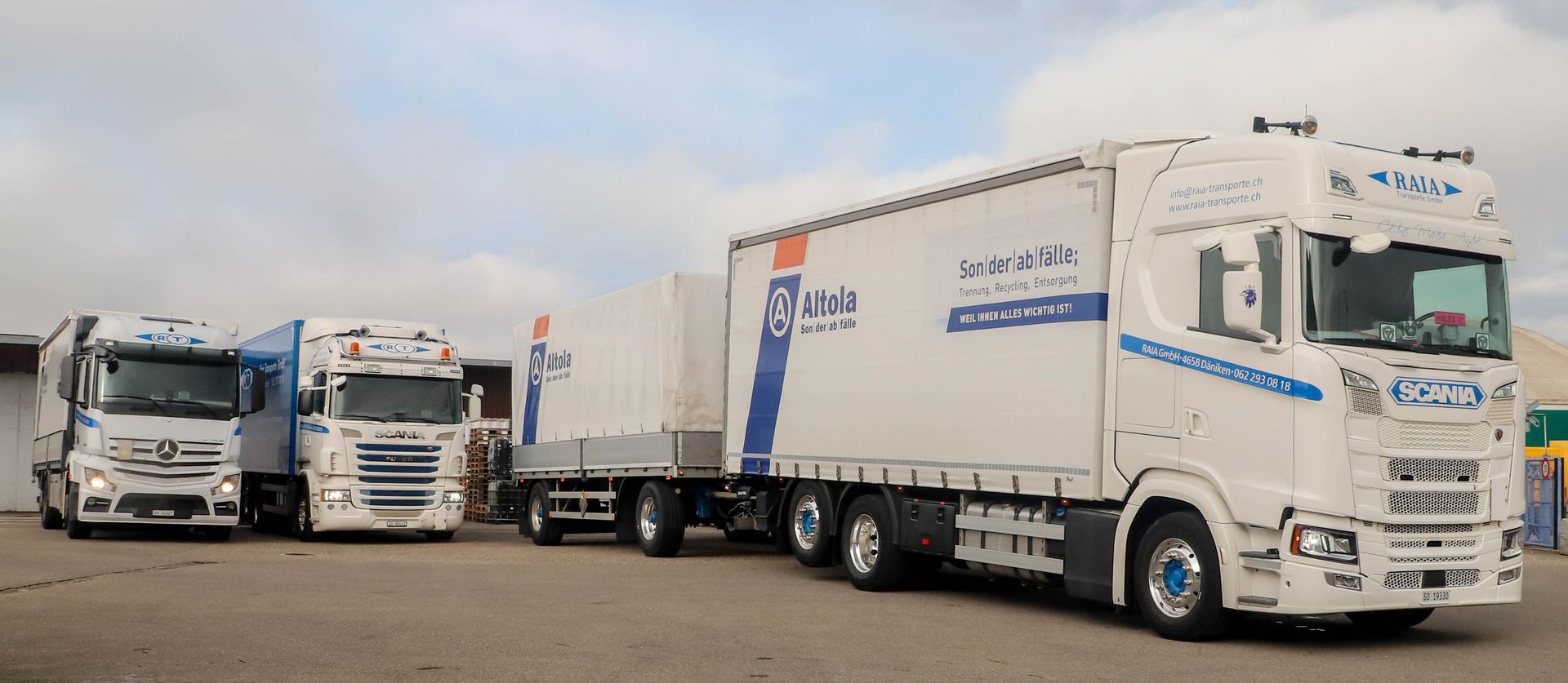 Weisse Scania-Lkw mit Abfallcontainern, geparkt im Freien unter bewölktem Himmel.
